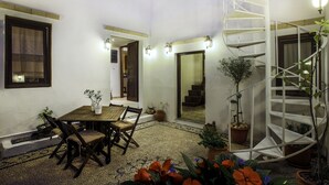 A courtyard with a wooden table and chairs, potted plants, a spiral staircase, and wall-mounted lighting. - Lindos Boutique Rooms - Adults Only (Rhodes)
