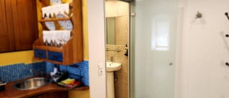 A kitchen with wooden cabinets and a blue tiled backsplash, leading to a bathroom with a glass shower door.
