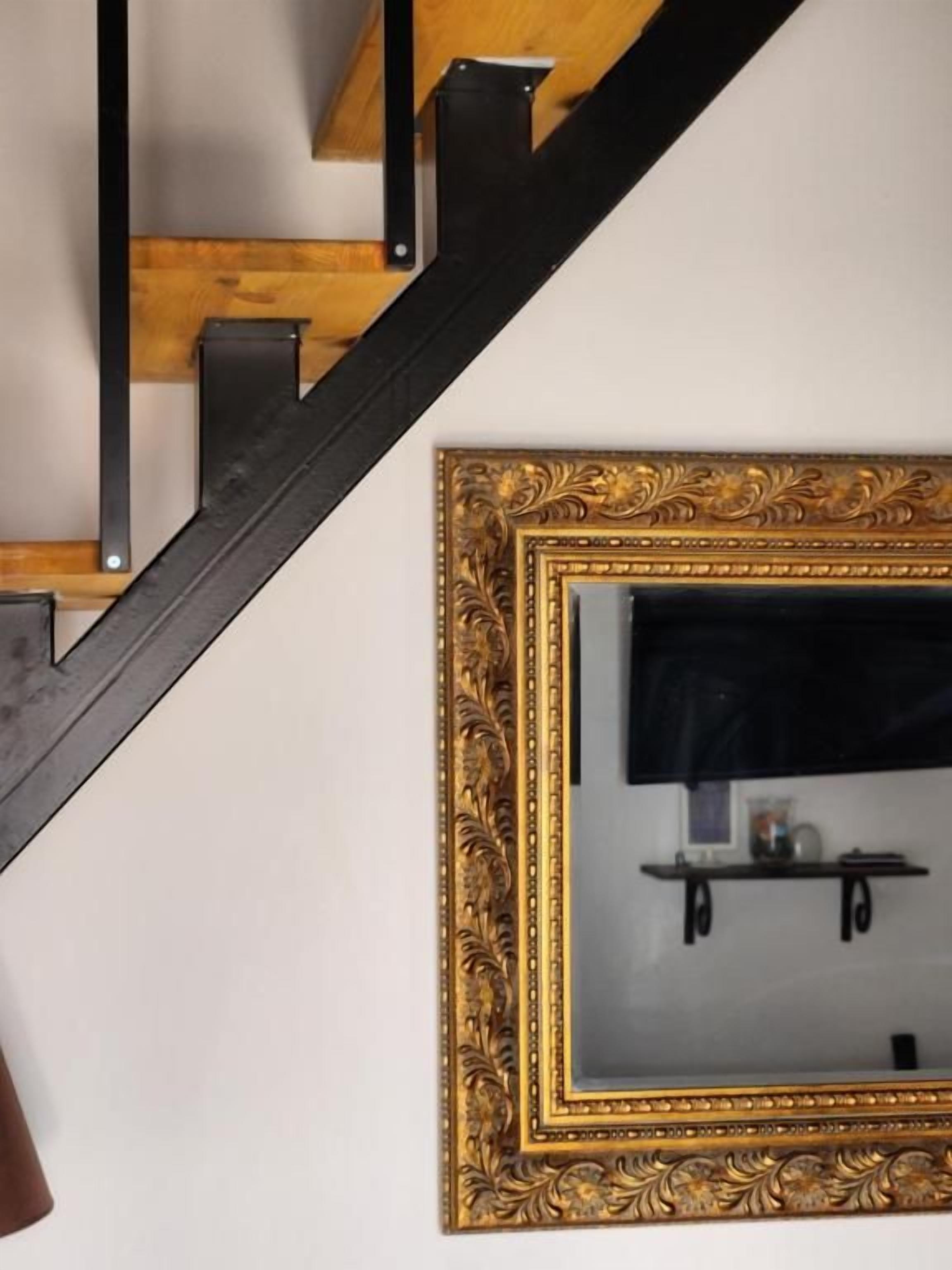 Una escalera con barandillas negras y un espejo con marco dorado en la pared.