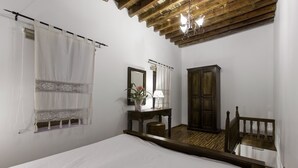 A bedroom with a wooden ceiling, a bed, a nightstand with a lamp, a mirror, and a wardrobe. - Lindos Boutique Rooms - Adults Only (Rhodes)