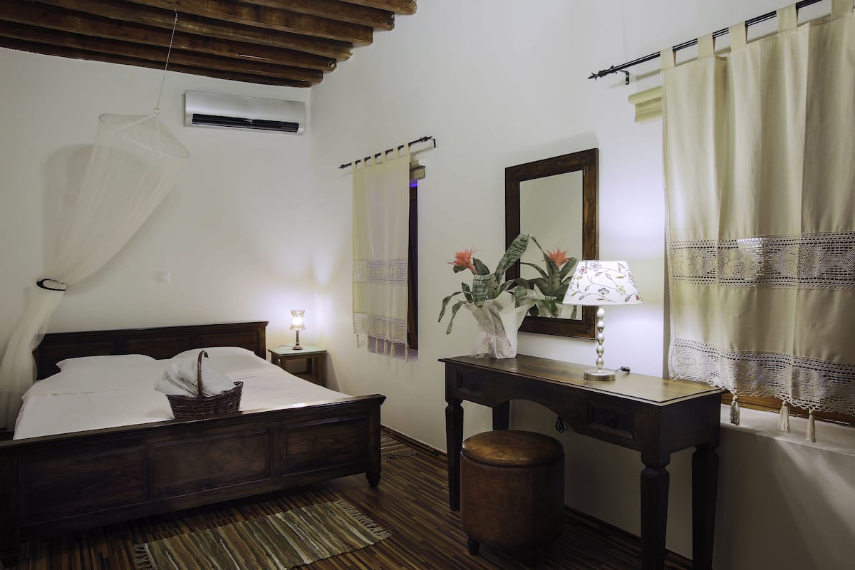 A bedroom with a wooden bed, bedside table, lamp, and a mirror.