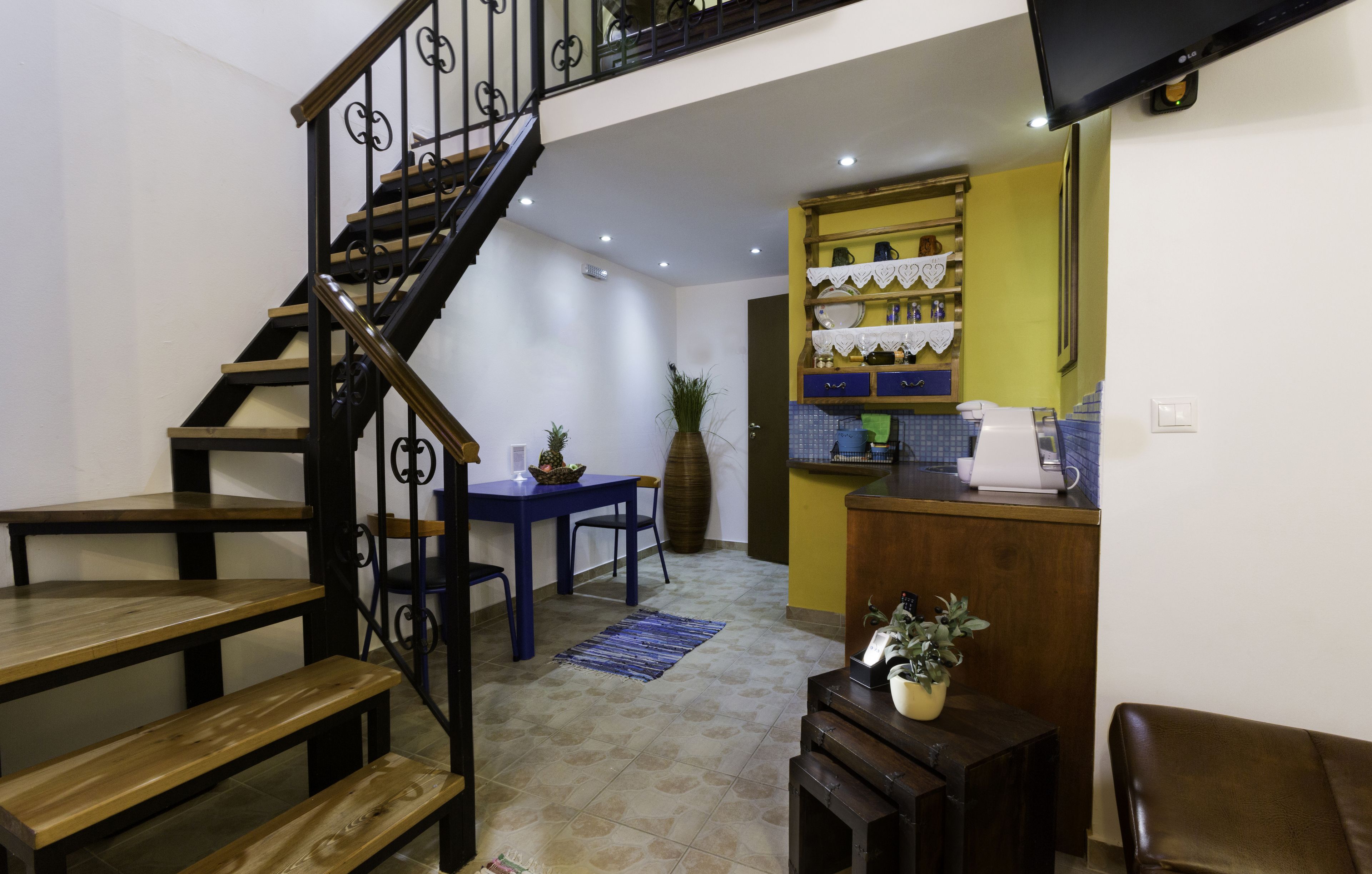 Un escalier menant à un niveau supérieur, un coin repas avec une table et des chaises bleues, et une cuisine avec des placards jaunes et un évier.