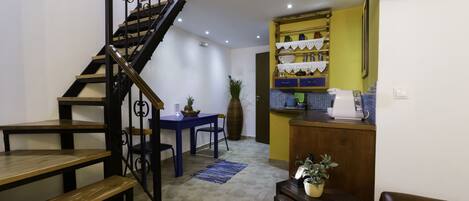 Un escalier menant à un niveau supérieur, un coin repas avec une table et des chaises bleues, et une cuisine avec des placards jaunes et un évier.