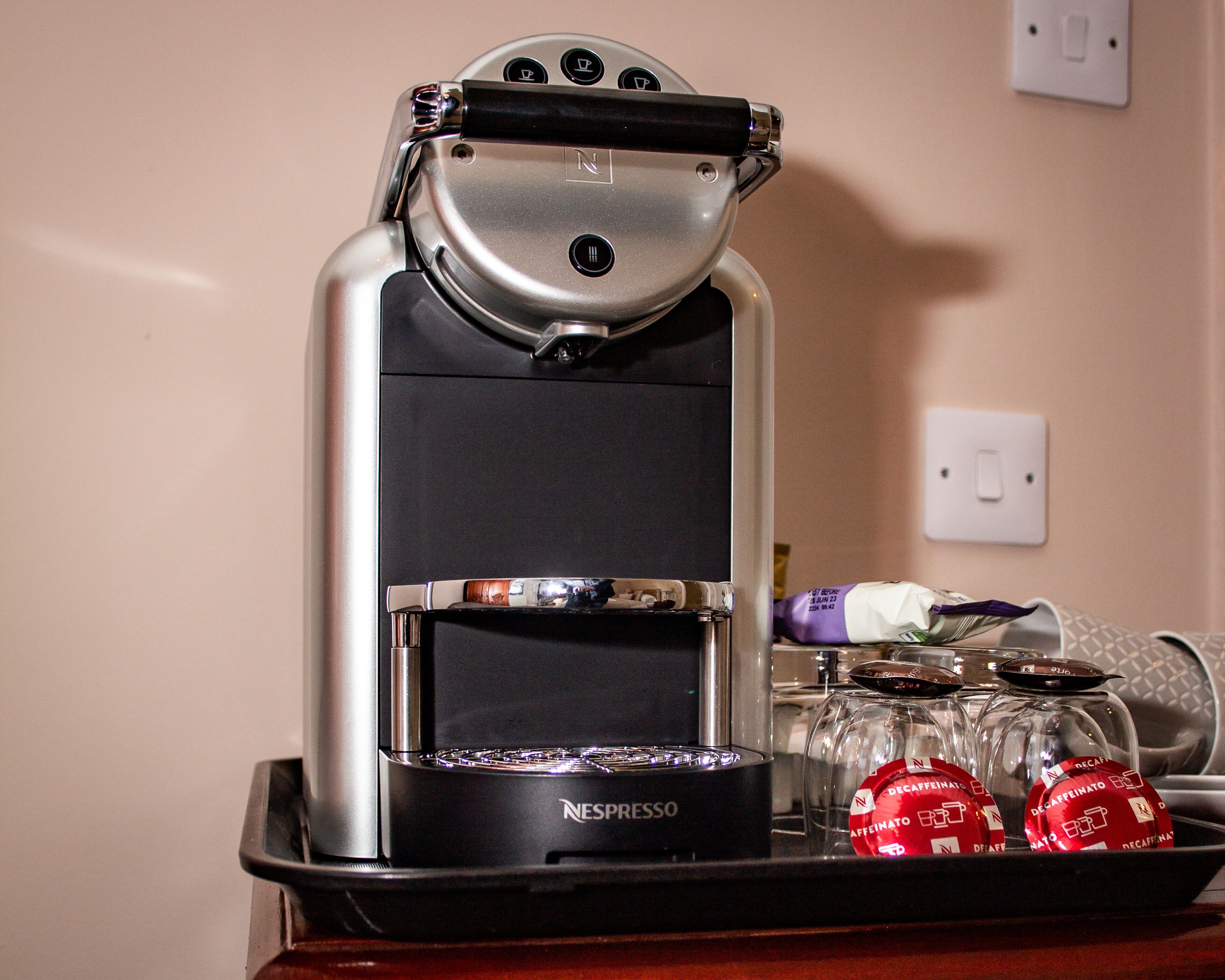 Une machine à café Nespresso, avec un présentoir de capsules de café et un verre d’eau.