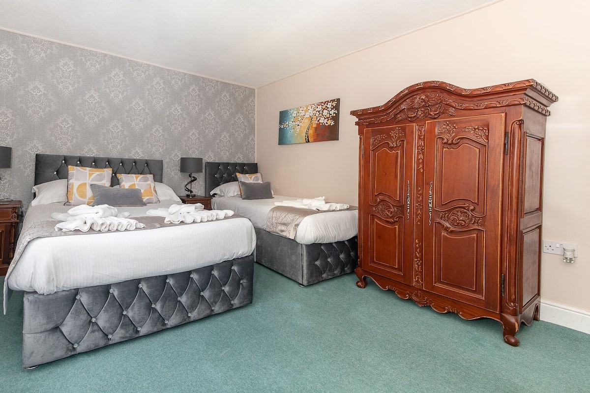 Ein Hotelzimmer mit einem großen Bett, einem kleineren Bett, einem Holzschrank und einem Bild an der Wand.