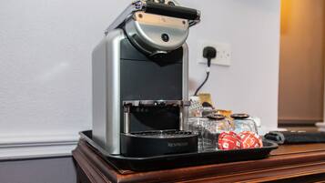 Une machine à café Nespresso posée sur un comptoir en bois, avec un plateau de capsules de café et une carafe en verre.