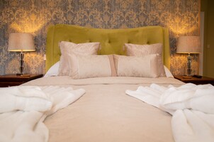 A neatly made bed with a green headboard, two bedside lamps, and a patterned wallpaper.