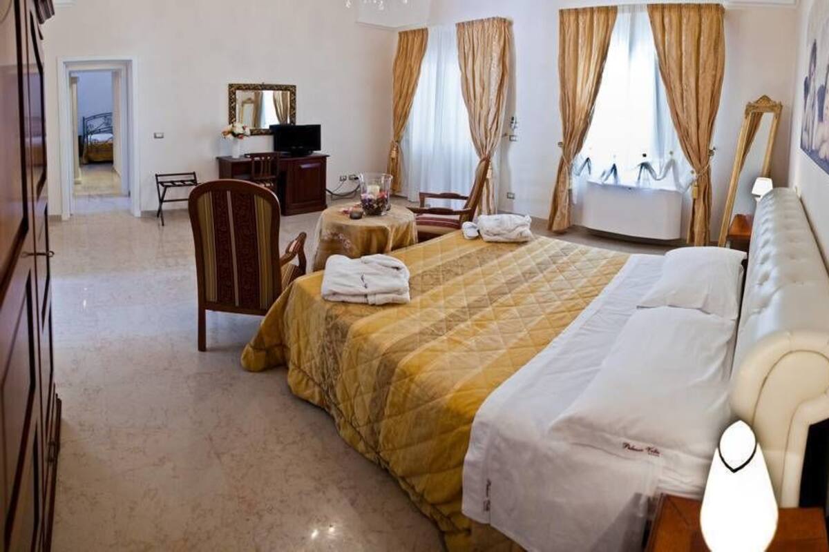 Une chambre d’hôtel avec un lit, un bureau, une chaise, une télévision et une fenêtre avec des rideaux.