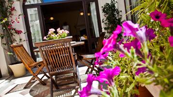 Een terras met houten stoelen en een tafel, omringd door potplanten en bloemen.