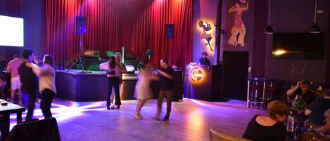 A dance floor with people dancing, a DJ booth, and a stage with curtains.