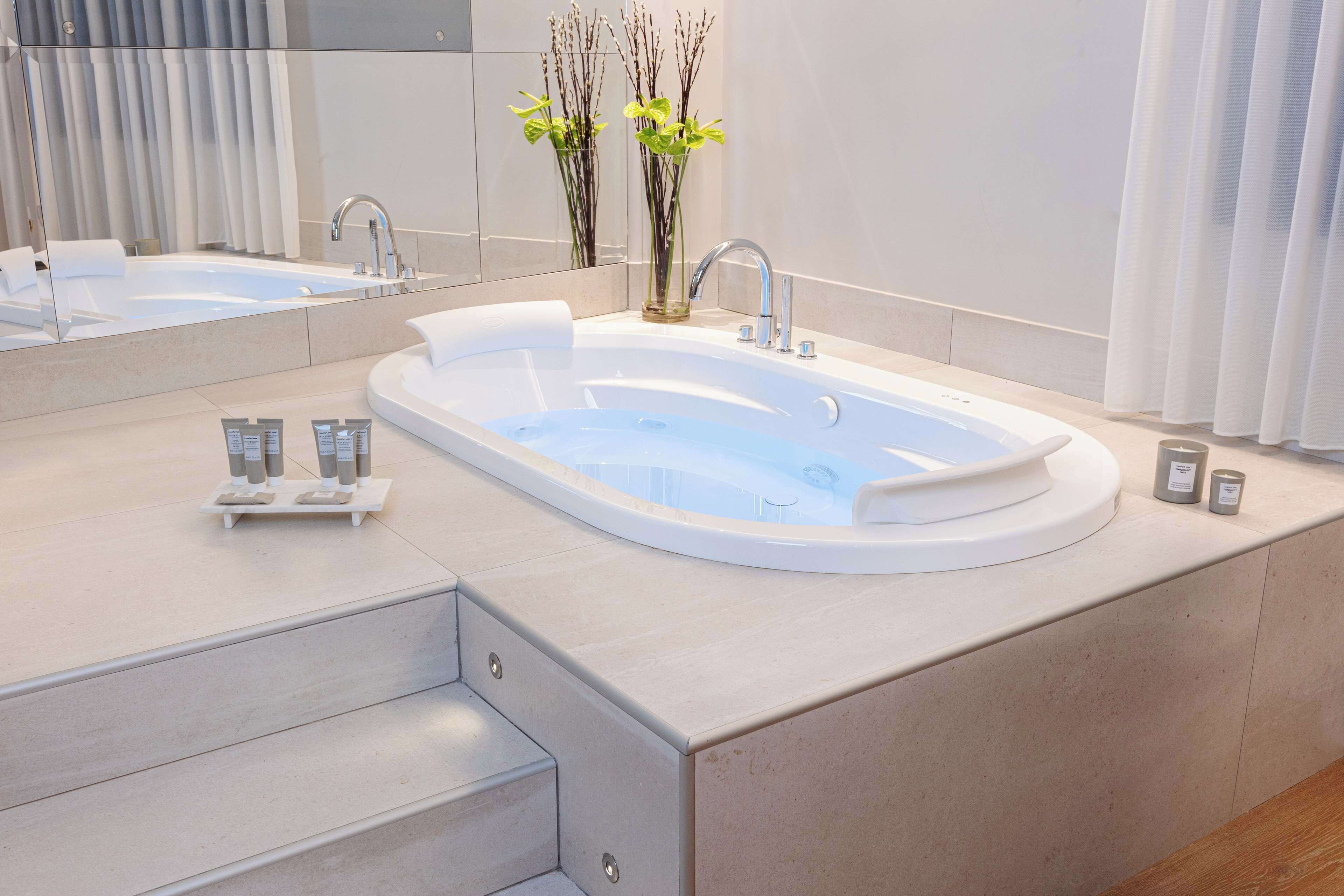 A modern bathroom with a freestanding bathtub, a large mirror, and a small plant arrangement.