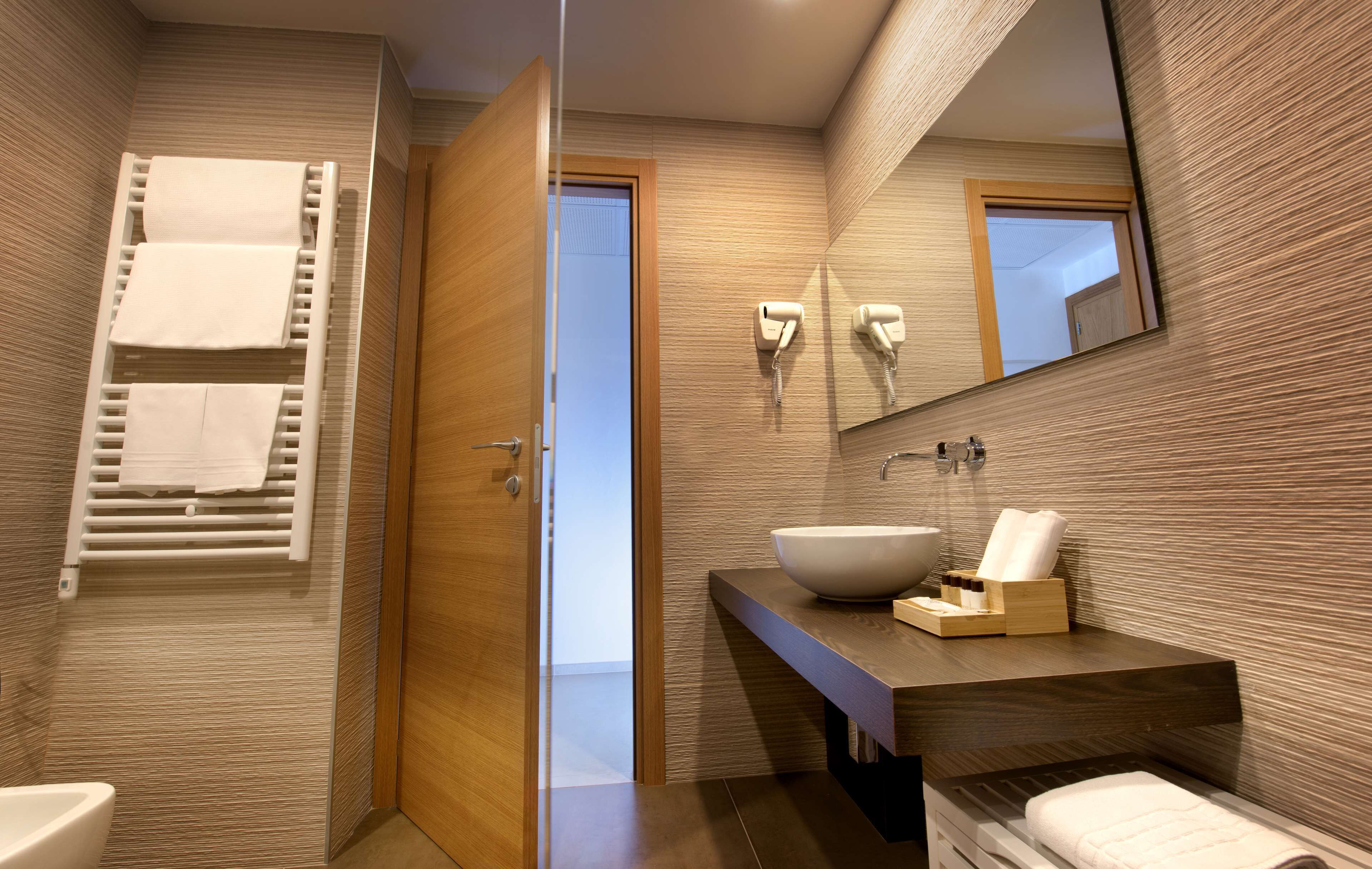Un baño moderno con cabina de ducha de vidrio, tocador de madera con un lavamanos grande y un perchero con varias toallas.