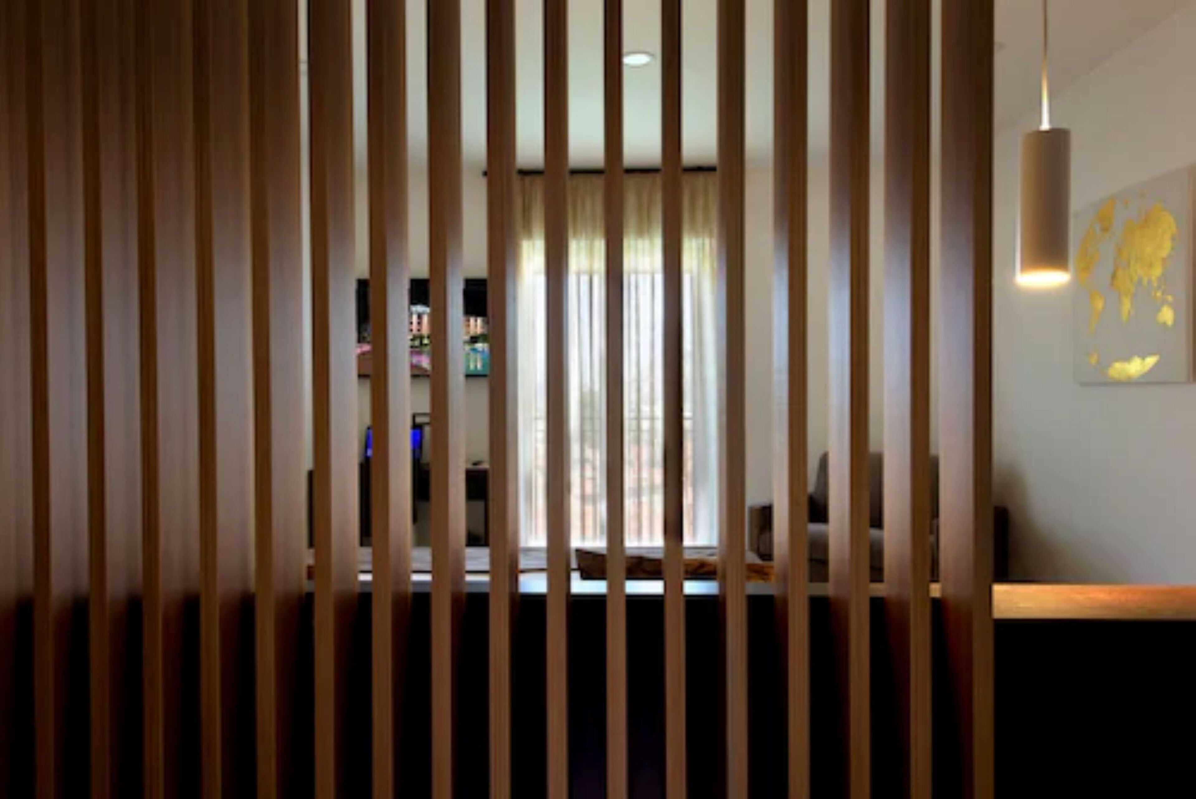 A room with a view through vertical blinds, a bookshelf, a hanging light fixture, and a wall-mounted artwork.