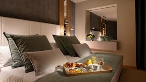 Una habitación de hotel moderna con una cama grande, varios almohadones, una bandeja con alimentos para el desayuno y un espejo que refleja la habitación.