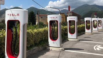 Une rangée de bornes de recharge réservées aux modèles Tesla 3, situées sur un parking avec des montagnes en arrière-plan.