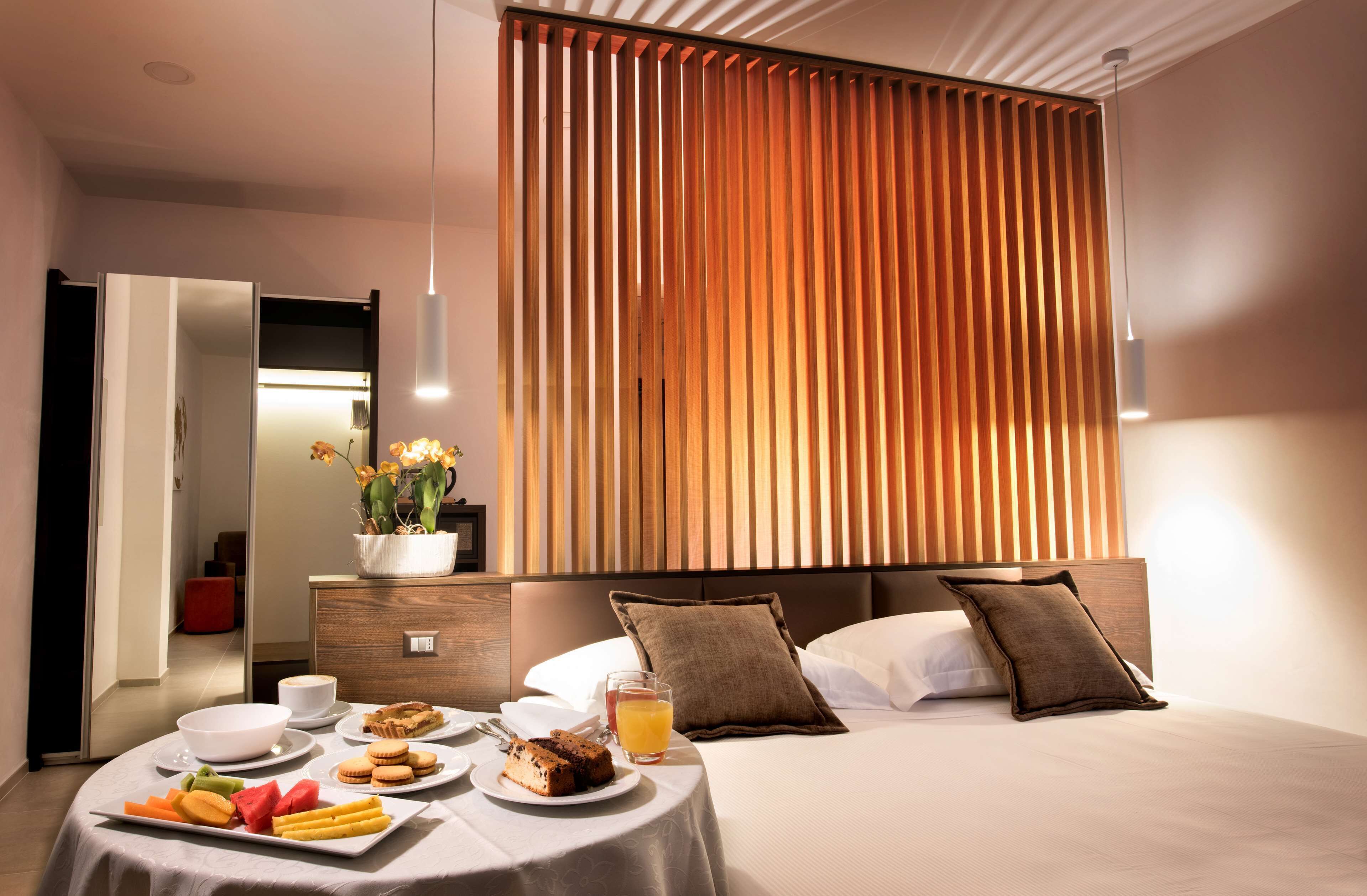 Una habitación de hotel moderna con una cama grande, una mesa de comedor con desayuno, y un panel de pared de madera vertical.