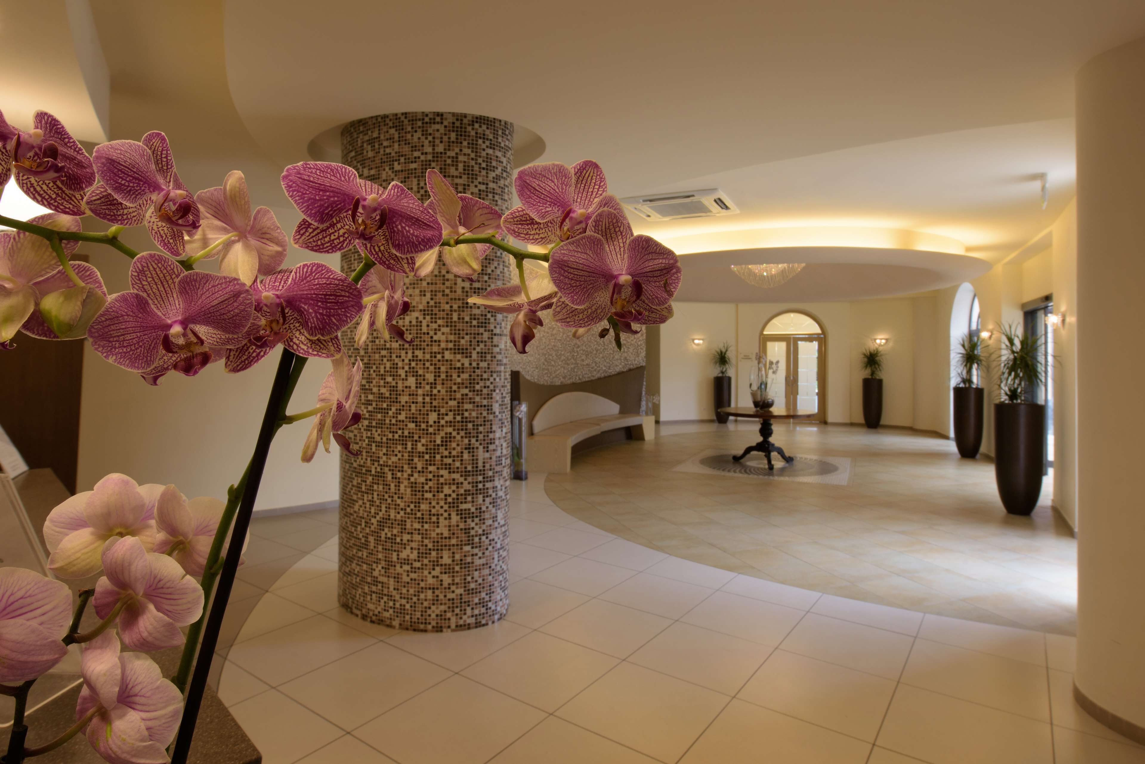 A spacious lobby with a large pillar, a staircase, and potted plants.