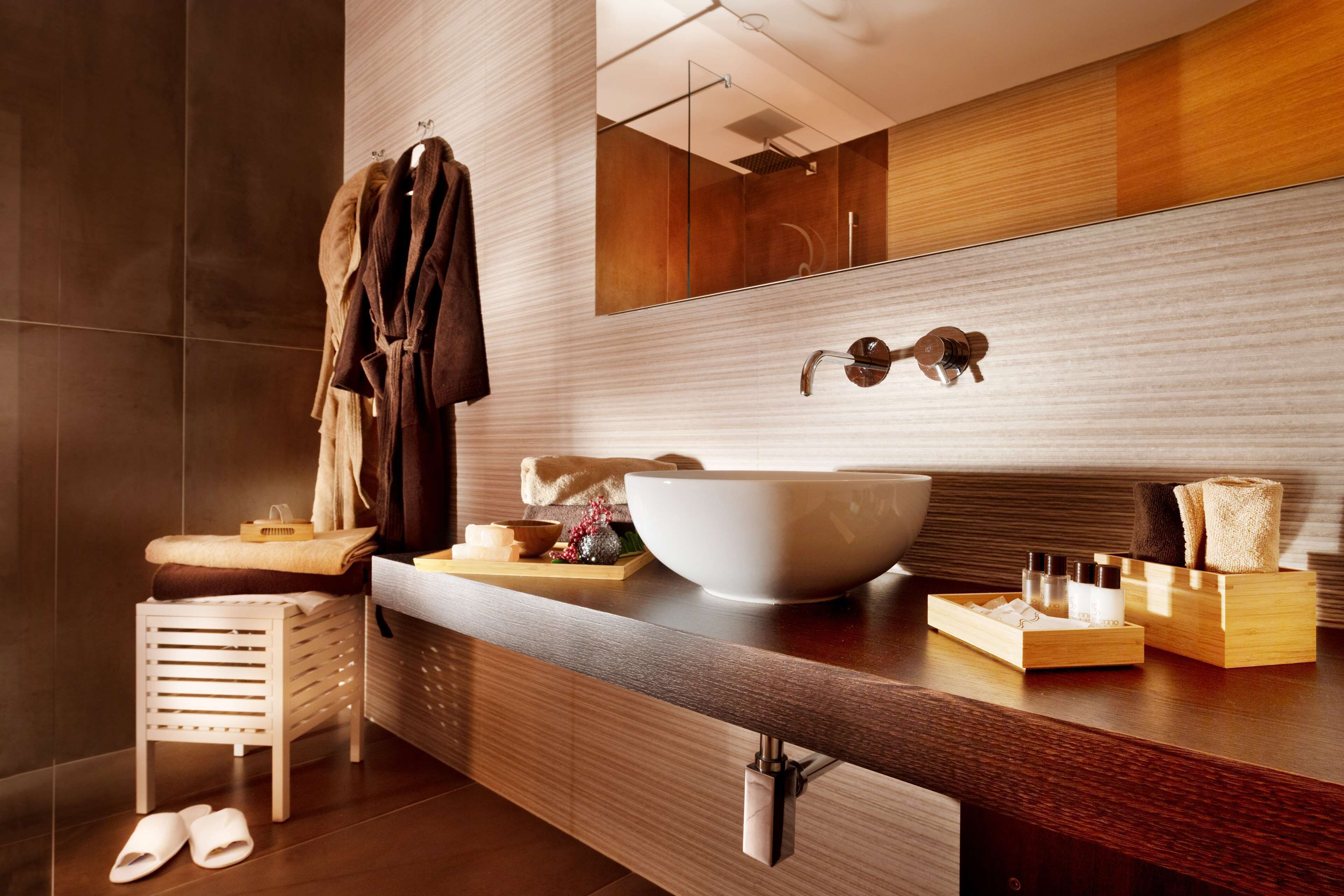 Une salle de bain moderne avec un grand lavabo blanc, un miroir et des meubles en bois. On y trouve des serviettes et des articles de toilette sur le comptoir.