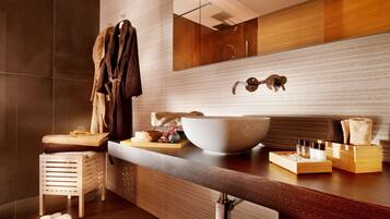 Une salle de bain moderne avec un grand lavabo blanc, un miroir et des meubles en bois. On y trouve des serviettes et des articles de toilette sur le comptoir.