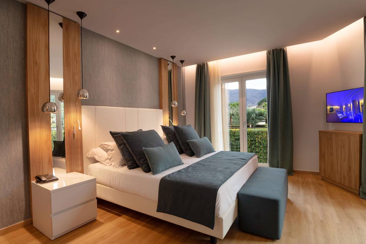 Un dormitorio moderno con una cama grande, mesitas de noche, un televisor y vistas a zonas verdes.