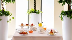 Una mesa de desayuno lista, con pasteles, tazas de café y un vaso de jugo de naranja.