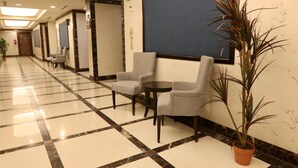 A hotel lobby with a checkered floor, seating area with chairs, a potted plant, and a large blue screen on the wall. - Platinum Park Serviced Apartments (Taif)
