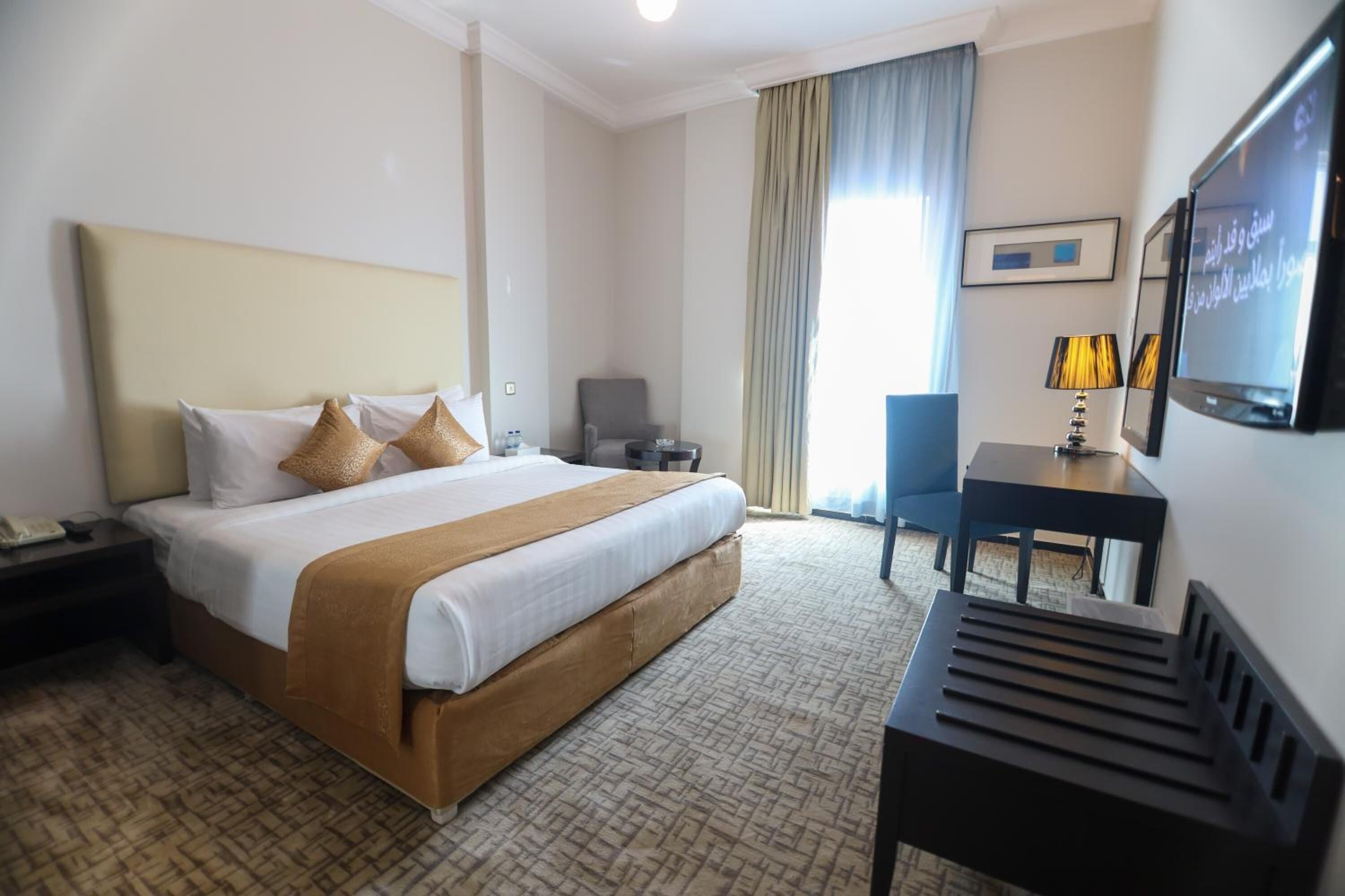 A hotel room with a large bed, a desk, a chair, a TV, and a window with curtains.