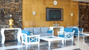 A modern lobby with a marble wall, a large sofa set, white chairs, and a flat-screen TV mounted on the wall. - Platinum Park Serviced Apartments (Taif)