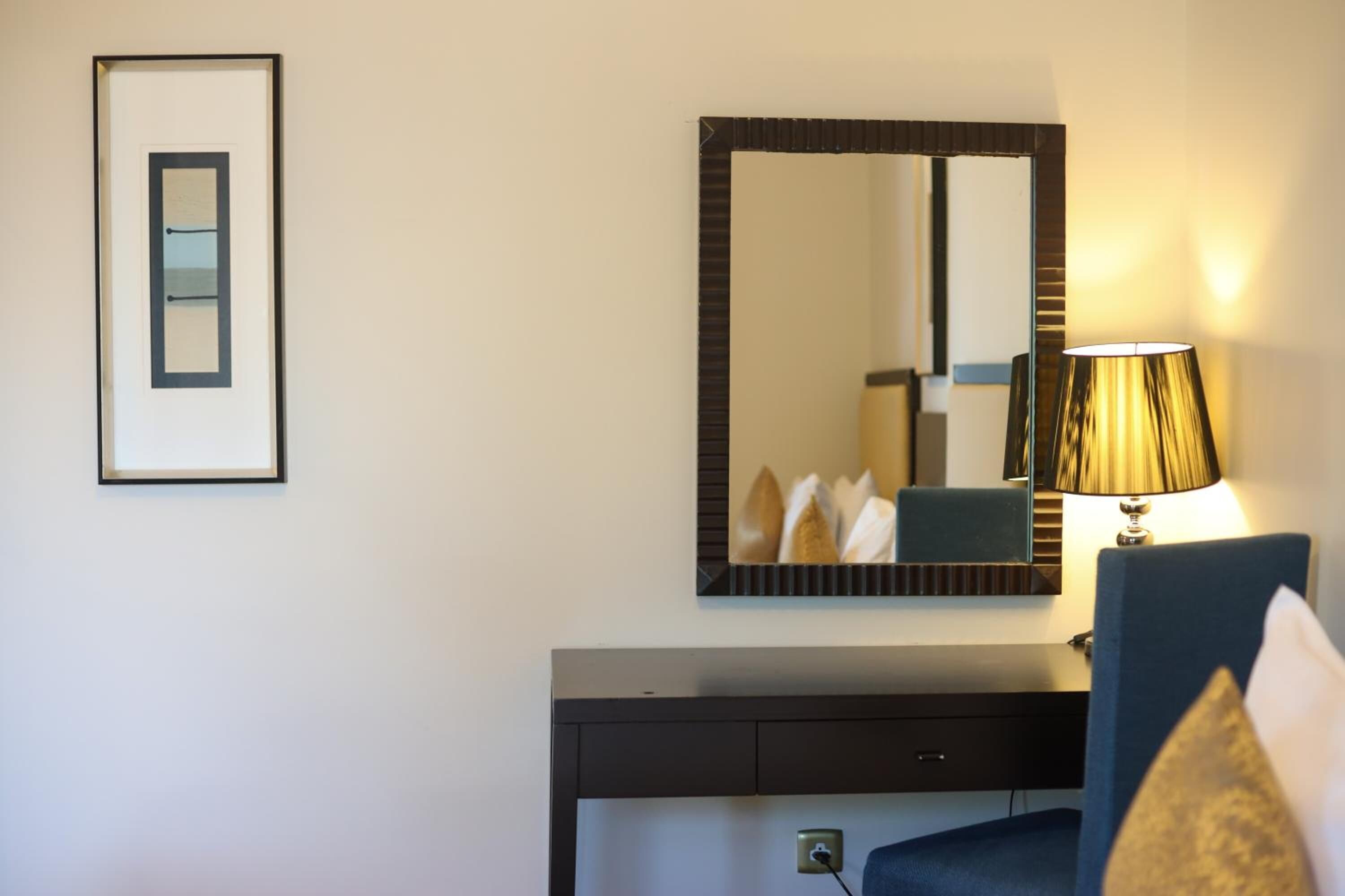 A hotel room with a large mirror, a framed picture, a bedside lamp, and a dark-colored dresser.