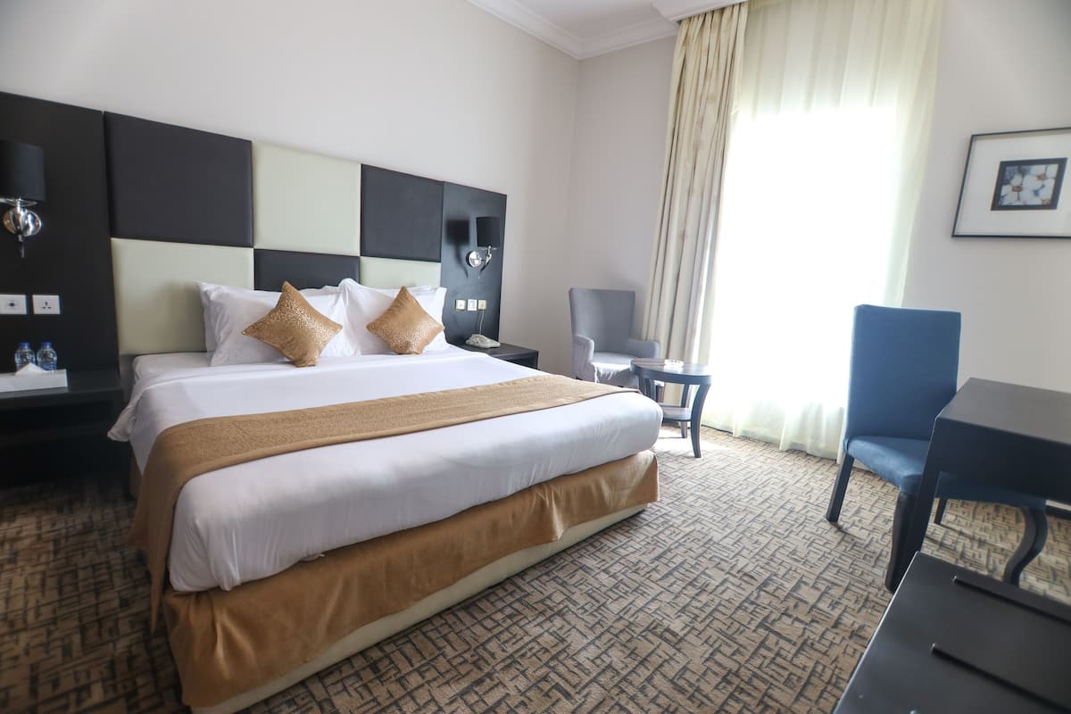 Una habitación de hotel con una cama grande, un escritorio, una silla y una mesita de noche con una lámpara.