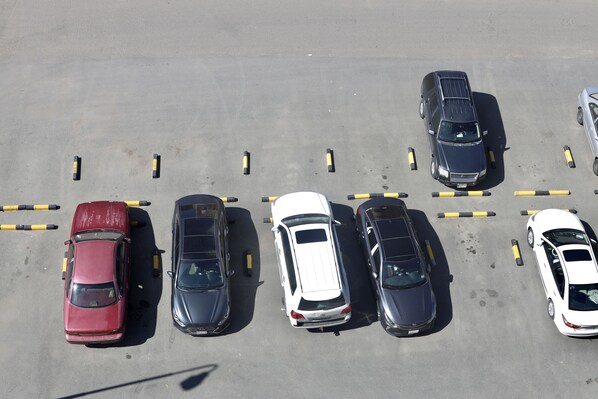 An aerial view of a parking lot with several cars parked in rows, marked by yellow and black lines.