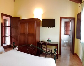 Un dormitorio con cama, armario de madera, escritorio con silla y televisor en la pared.