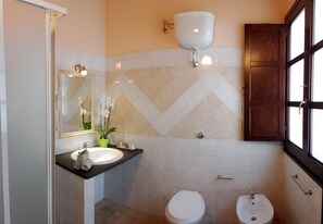 Un baño con lavamanos, inodoro, bidé y un espejo con una orquídea en maceta.