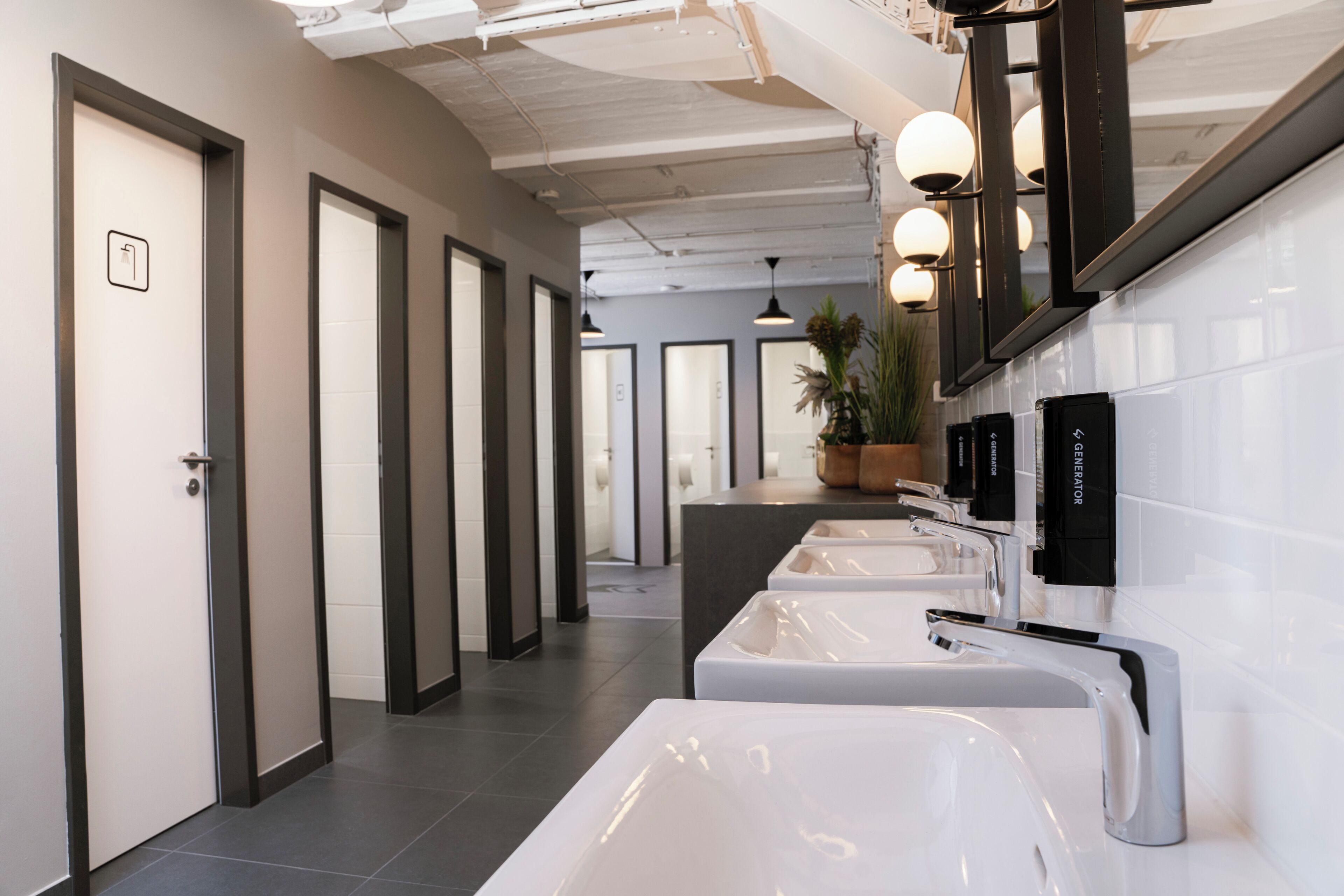 A modern bathroom with multiple sinks, a large mirror, and a potted plant.
