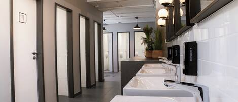 A modern bathroom with multiple sinks, a large mirror, and a potted plant.