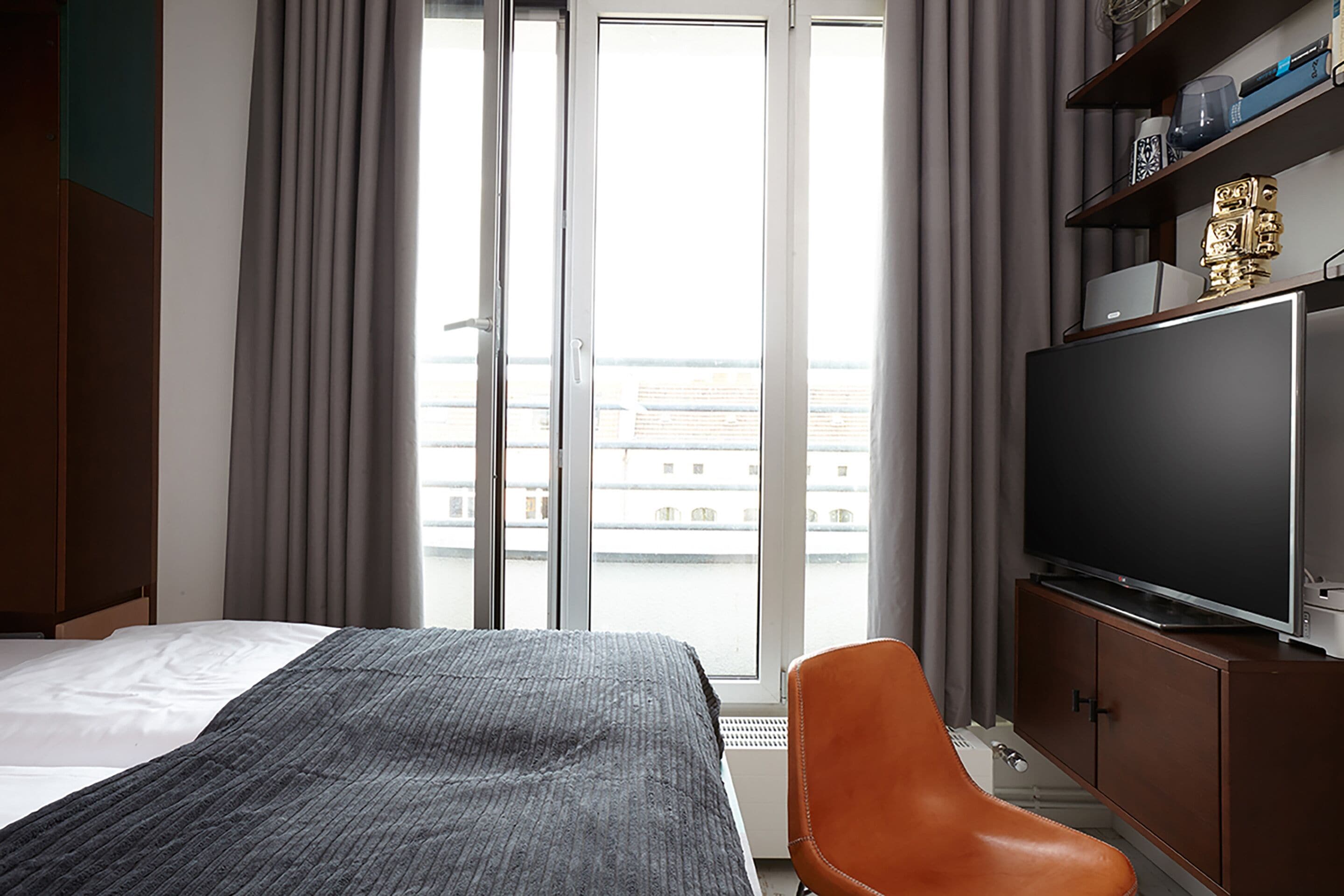 Habitación de hotel con cama, televisor, escritorio y vistas a la ciudad desde la ventana.