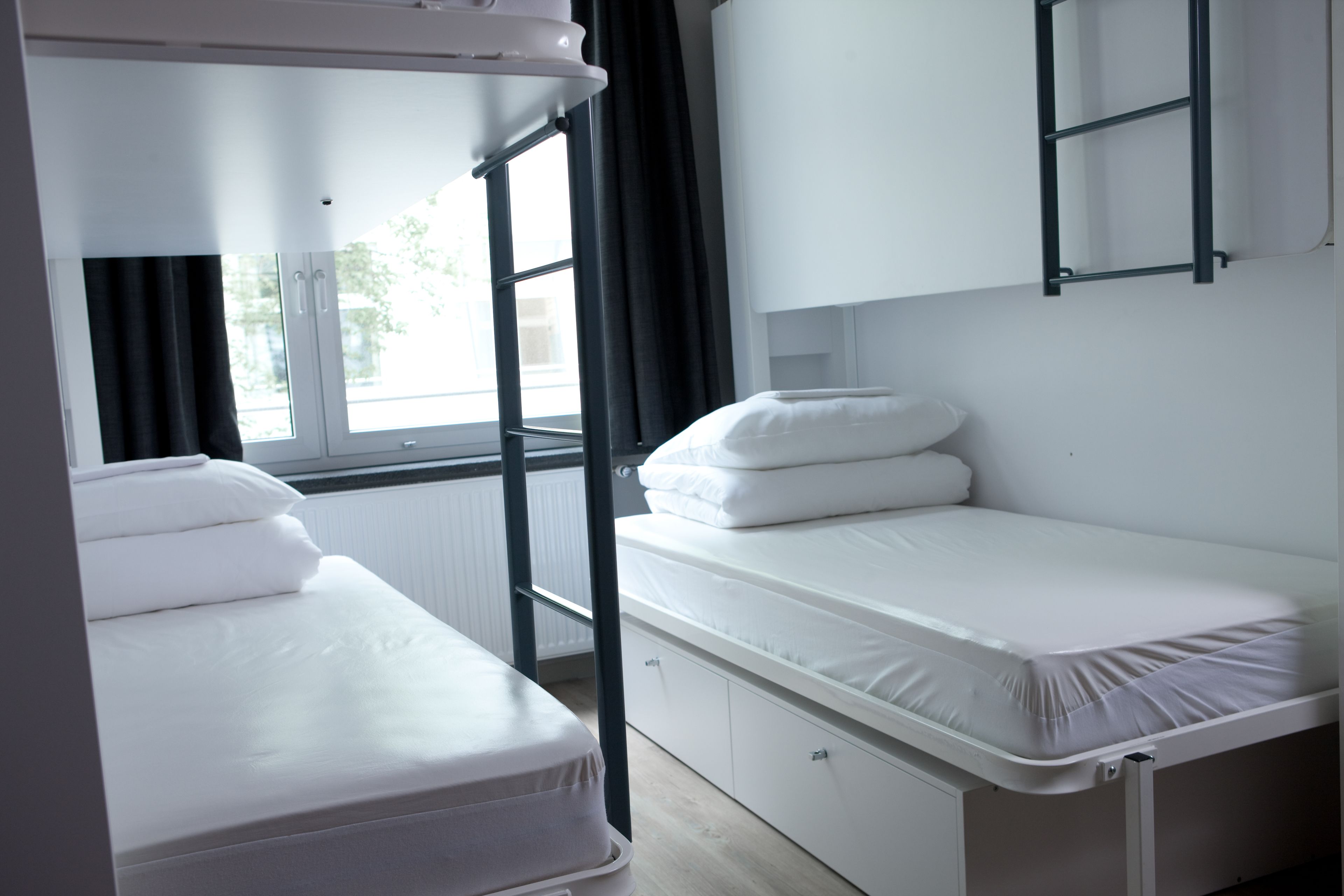 Ein Etagenbett mit Schreibtisch und einer kleinen Ablage, ein Fenster mit Vorhängen und eine Heizung.
