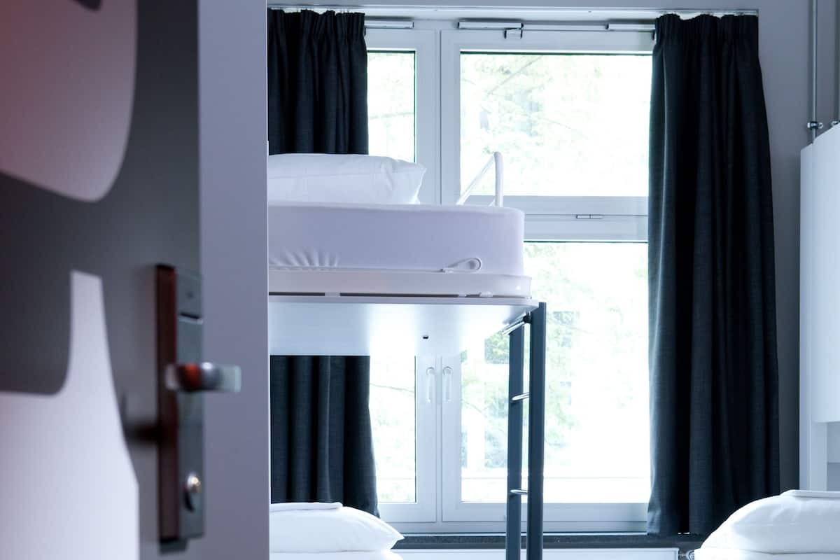 A hotel room with bunk beds, a window with curtains, and a wooden floor.