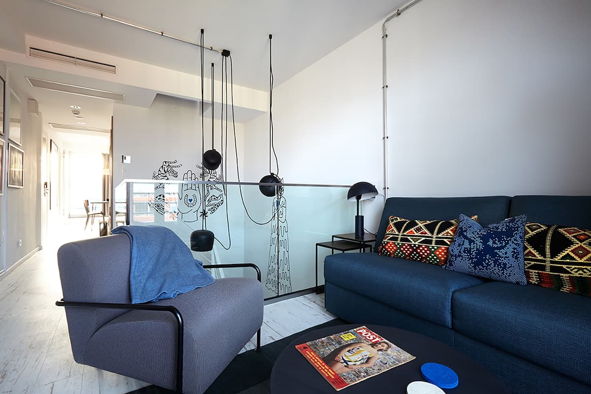 A modern living room with a sofa, armchair, and coffee table. There is a dining area in the background with a table and chairs.