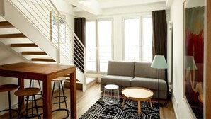 Una sala de estar moderna con una escalera, un sofá gris, una mesa de centro redonda y una alfombra estampada.