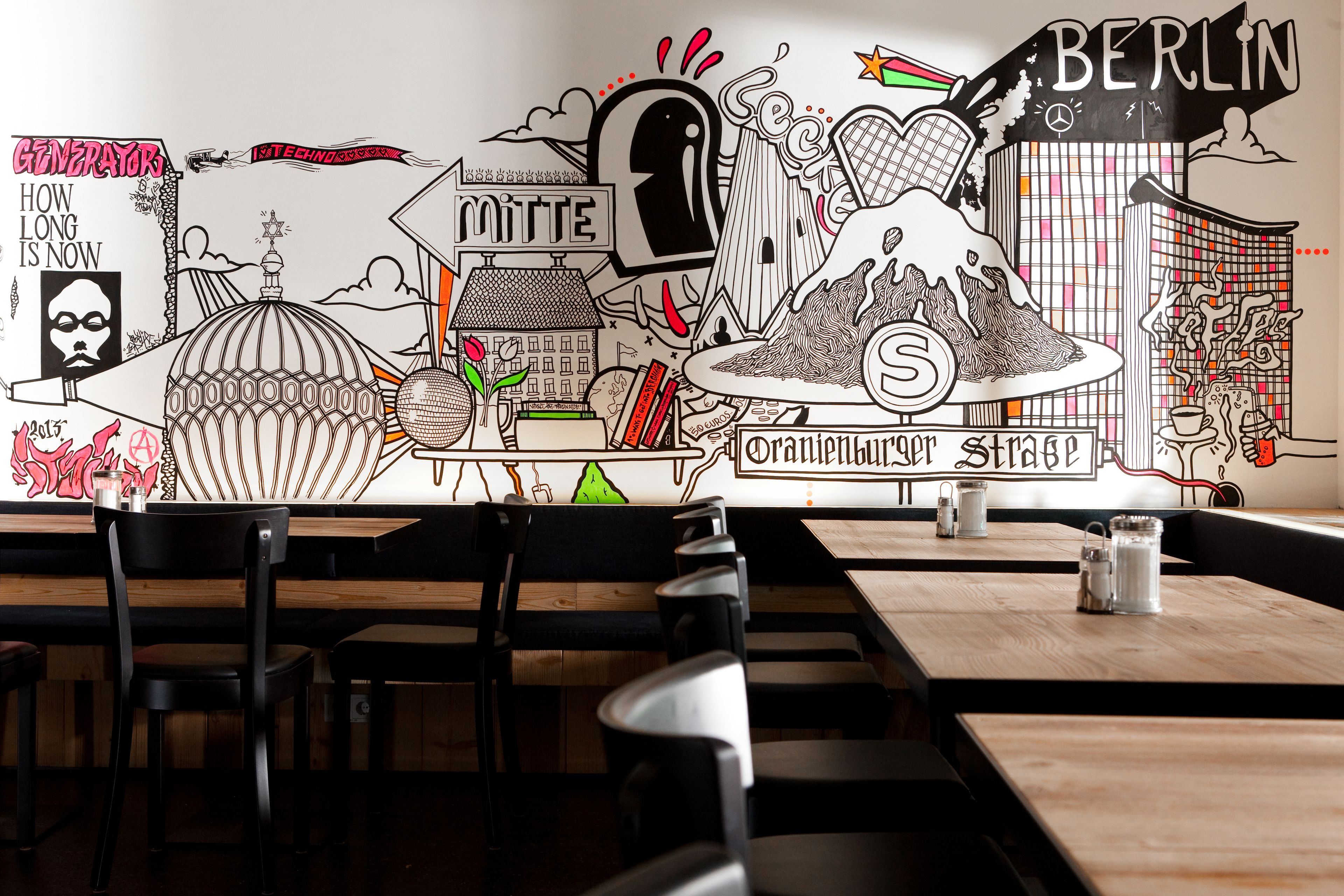 Ein Restaurantinneres mit Holztischen und schwarzen Stühlen, das ein Wandgemälde mit verschiedenen Illustrationen und Texten zeigt.