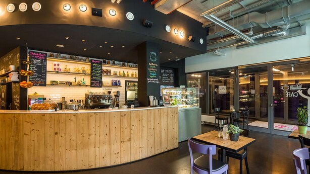 Un café moderno con mostrador de madera, zona de estar y carteleras del menú a la vista.
