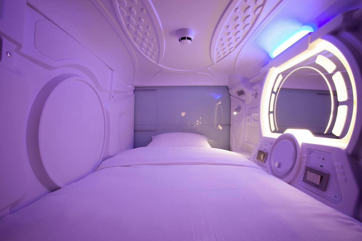 A modern, minimalist room with a large bed, a circular window, and built-in speakers.