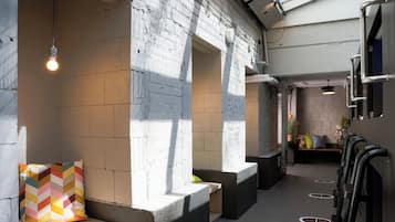 A modern interior with white brick walls, a seating area with a colorful cushion, and a row of black luggage racks.