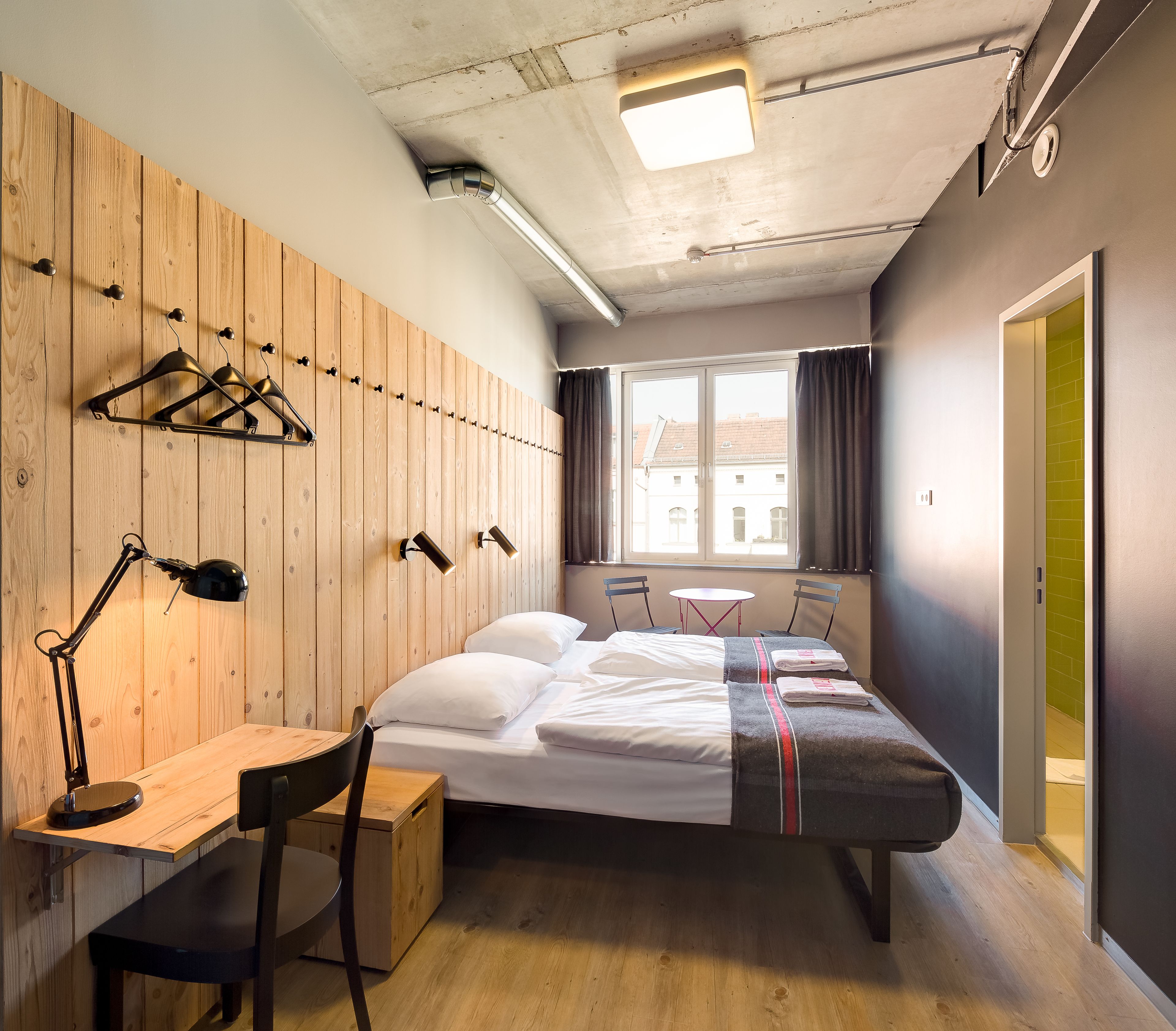 Habitación de hotel con cama, escritorio, silla y ventana con vistas a edificios.