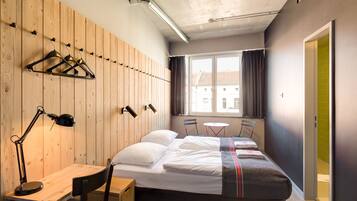 Habitación de hotel con cama, escritorio, silla y ventana con vistas a edificios.