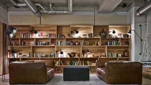 Un rincón acogedor para leer, con sofás de cuero, un otoman central y una amplia estantería de madera llena de libros.