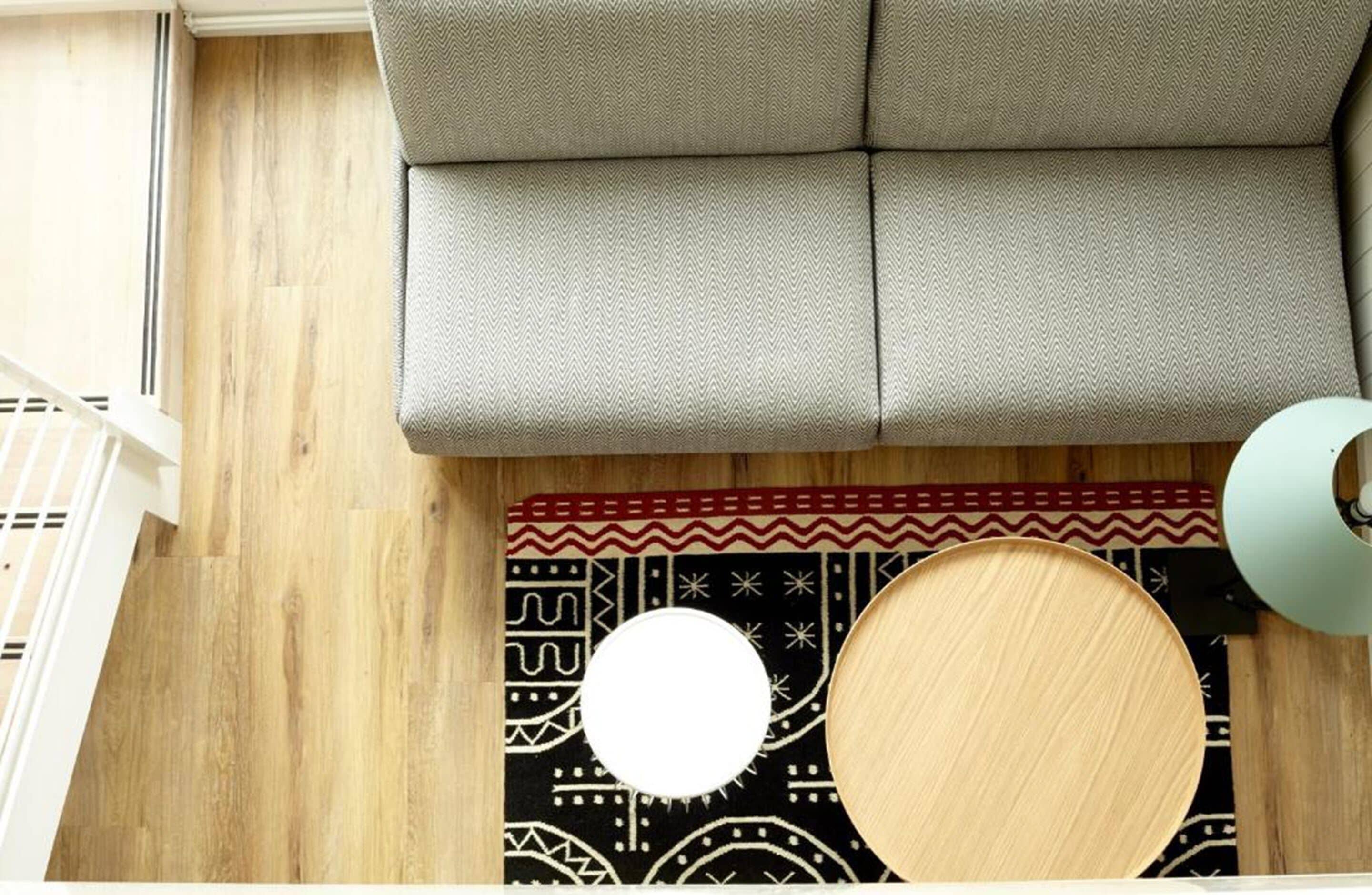 A top-down view of a room with a sofa, a patterned rug, and a circular wooden object on the floor.