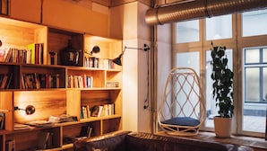 Una sala de estar acogedora con un sofá de cuero, estanterías de madera, un sillón de mimbre y una planta en maceta junto a un ventanal amplio.