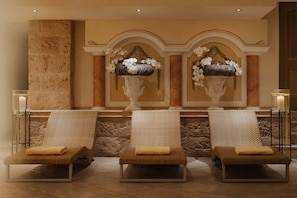 Un espacio de spa con tres sillones de descanso, un muro de piedra y dos jarrones grandes con flores blancas.